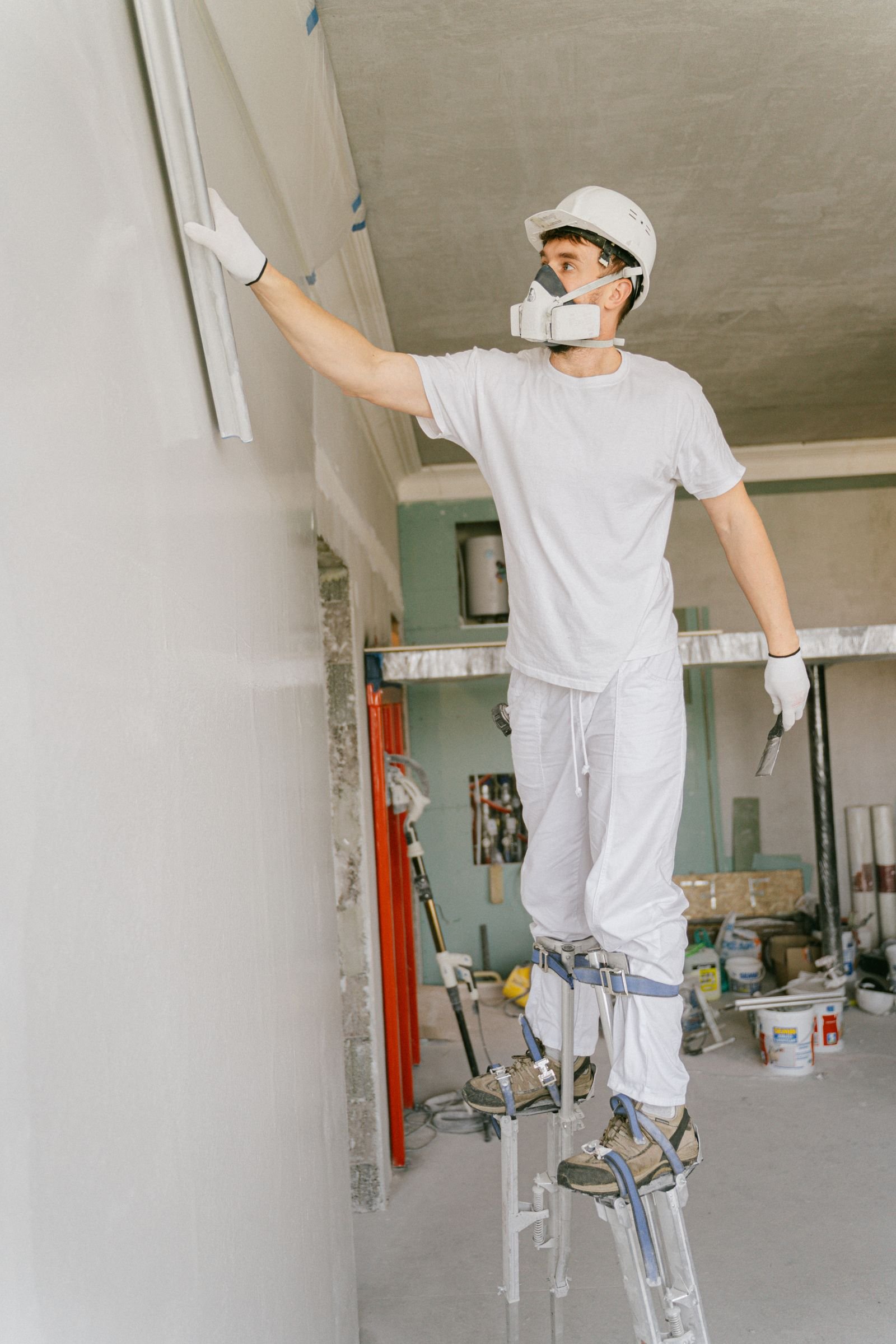 Worker in white workwear finishing a high interior wall - illustrative stock photo