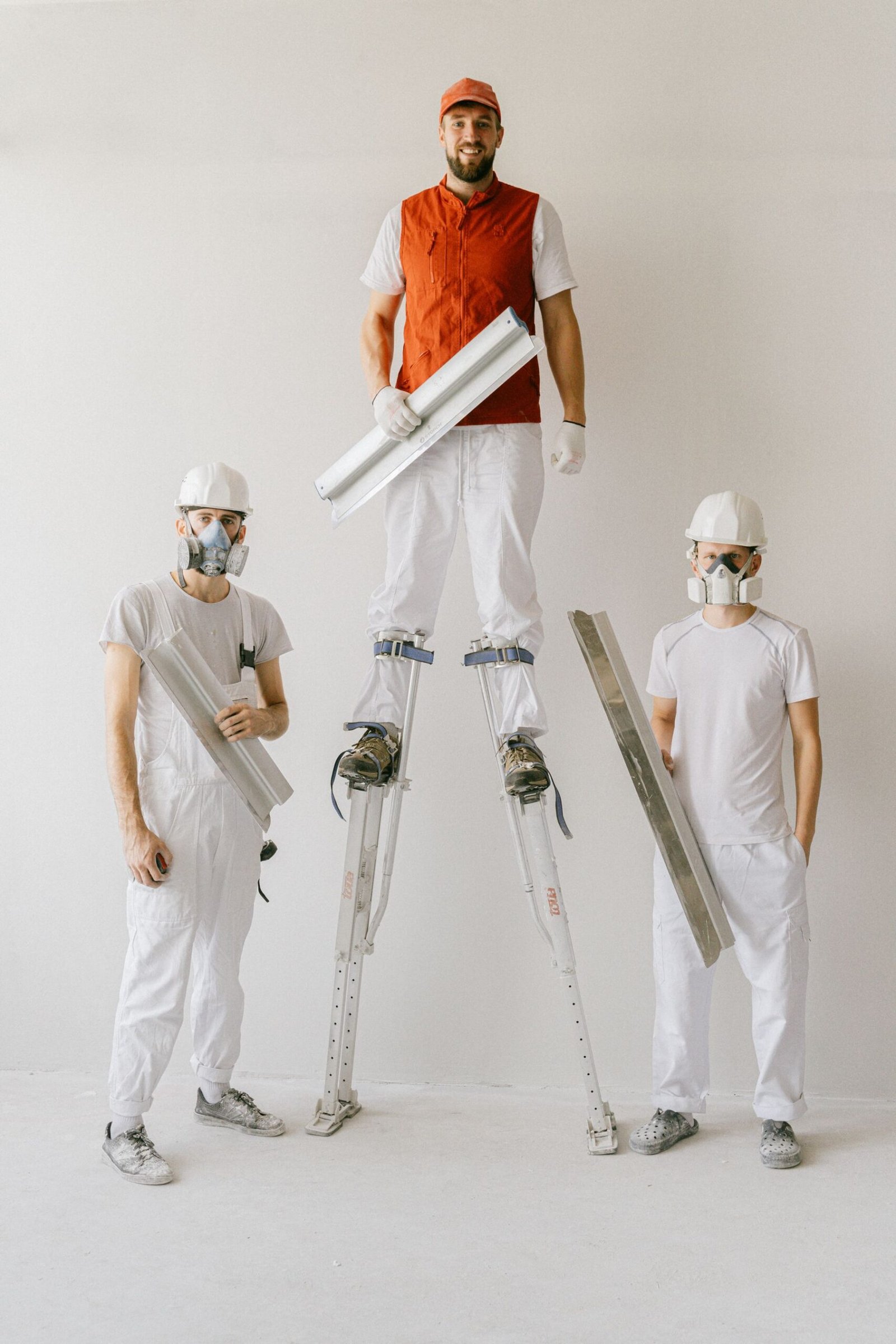 Uniformed drywall workers using stilts to finish tall walls - illustrative stock photo