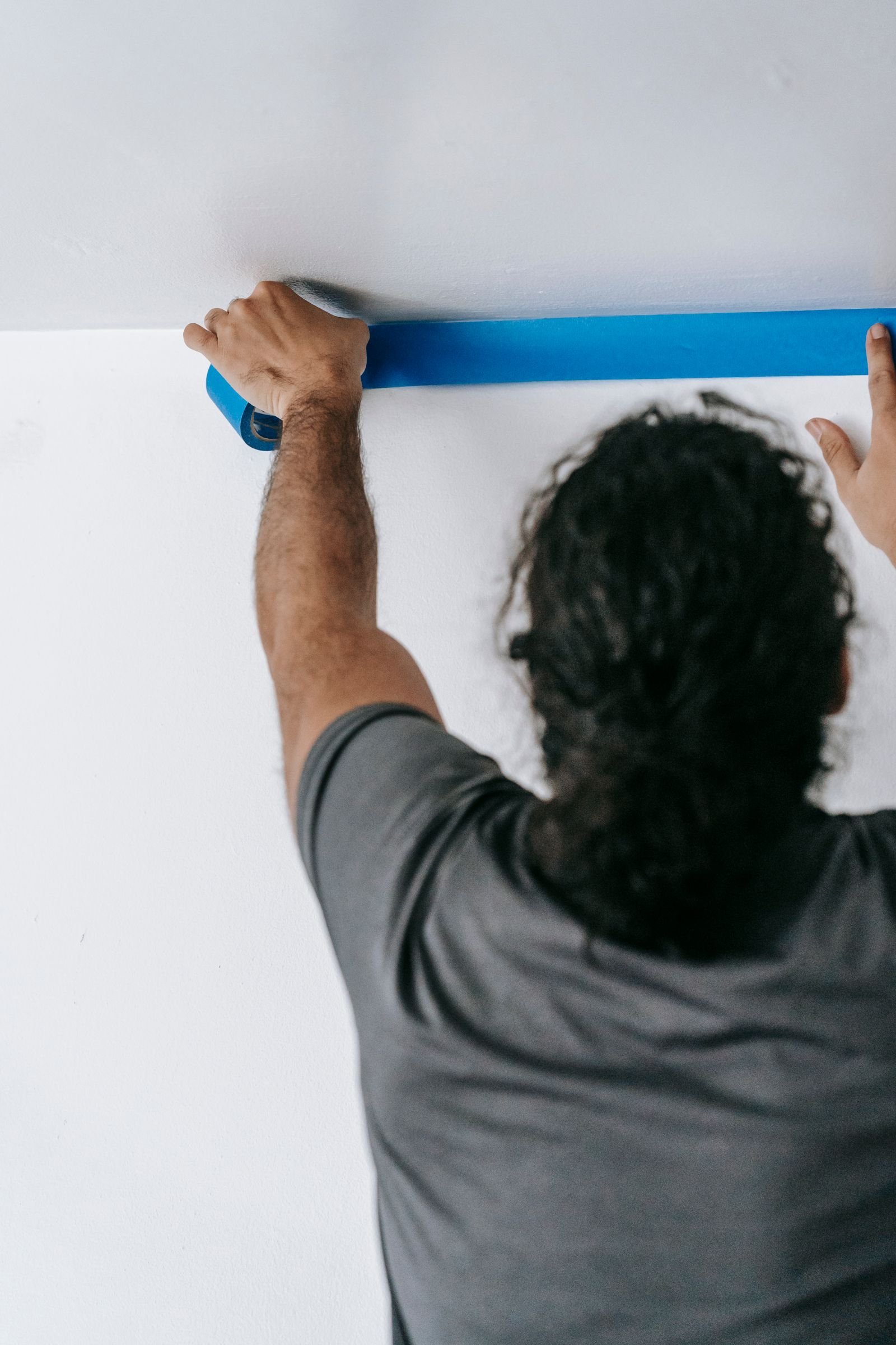 Worker applying masking tape along the ceiling before painting - illustrative stock photo