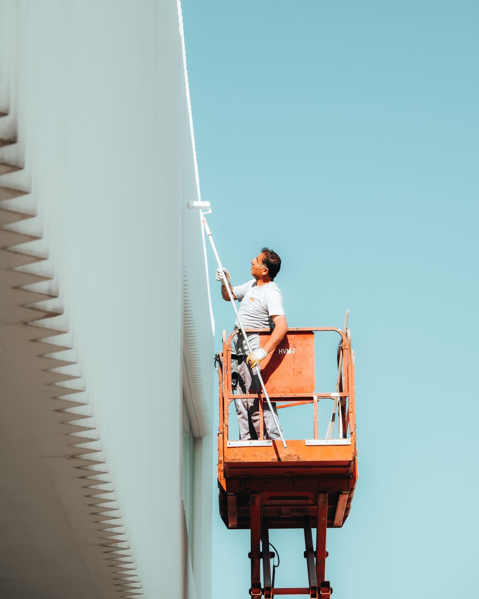 Worker on an elevated platform painting a building exterior - illustrative stock photo