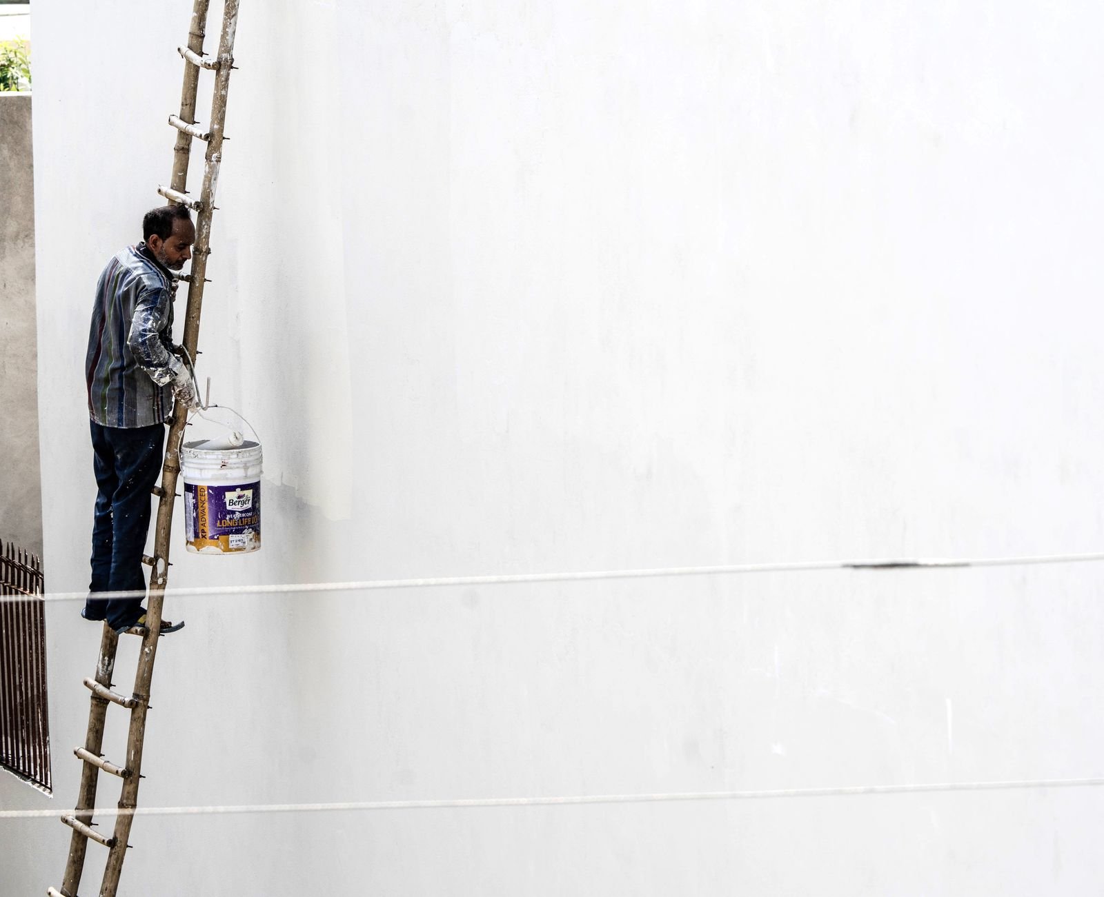 Worker painting a large white exterior wall from a ladder - illustrative stock photo