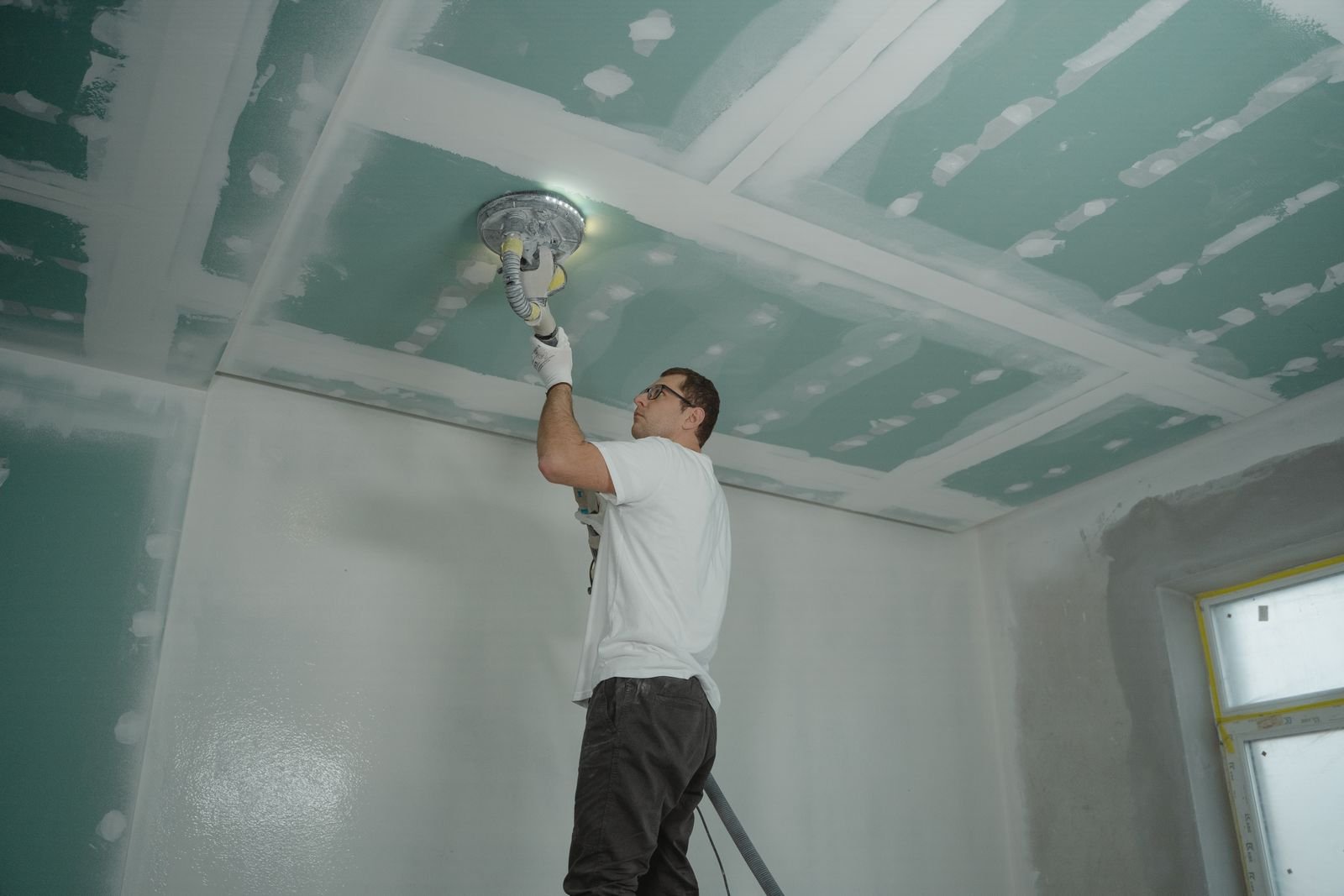Worker sanding an interior ceiling during renovation - illustrative stock photo