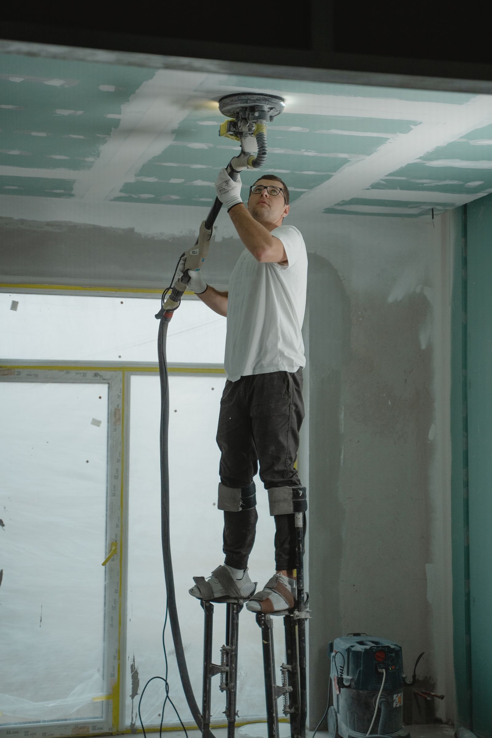 Worker on stilts sanding a ceiling before finishing - illustrative stock photo