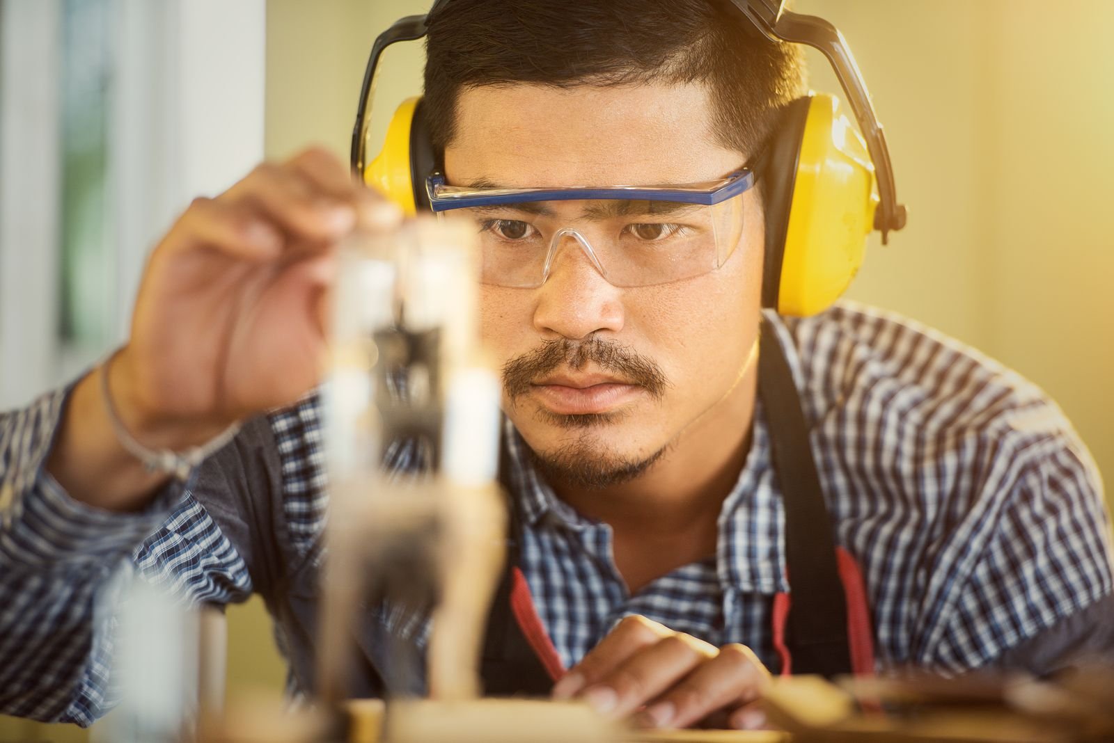 Carpenter in protective equipment measuring a piece of wood - illustrative stock photo