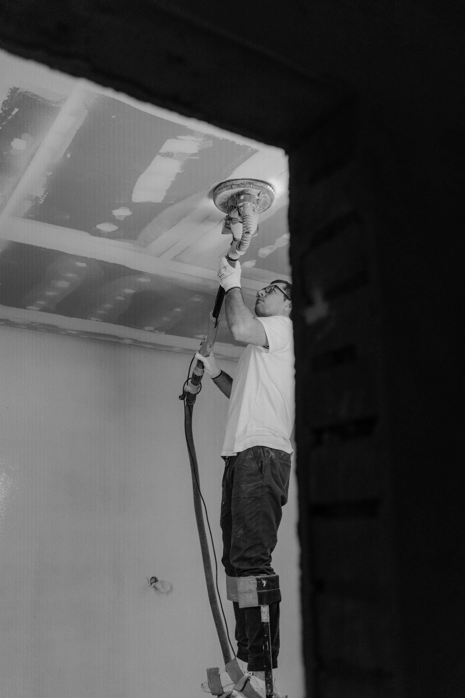 Black and white photograph of a worker sanding an interior ceiling - illustrative stock photo