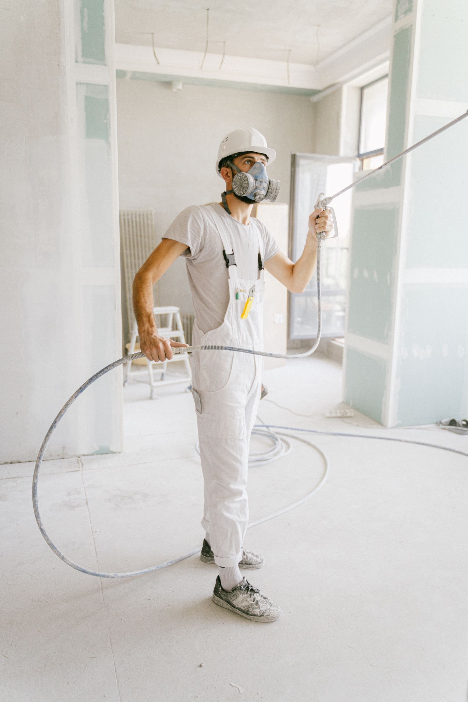 Painter in protective white workwear applying a spray finish - illustrative stock photo