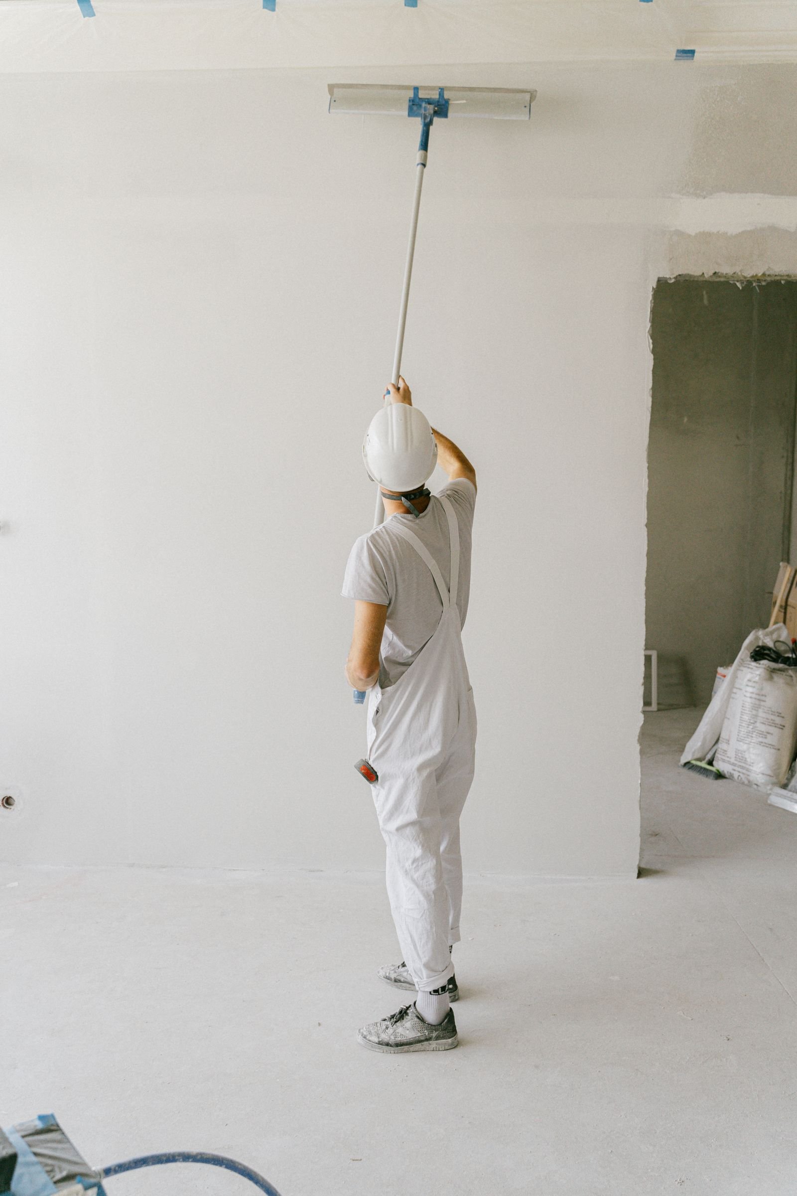 Painter in work overalls applying paint to an interior wall with a roller - illustrative stock photograph